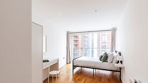 A bedroom with a bed, a desk, and a window with curtains. - Bright Battersea Apartment (London)