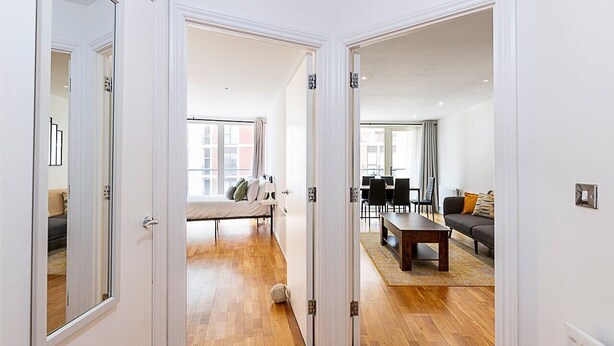 A modern apartment with a wooden floor, a dining area with a table and chairs, a sofa, and a bed with a window view. - Bright Battersea Apartment (London)