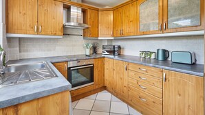 A kitchen with wooden cabinets, a stainless steel sink, a microwave, and a toaster. - Chester home only 2km from famous Races and Roman City, sleeps 6 by Restfully (Chester)