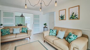 A spacious living room with two beige sofas, green patterned cushions, and a large window with a view of the outdoors. - Chester home only 2km from famous Races and Roman City, sleeps 6 by Restfully (Chester)