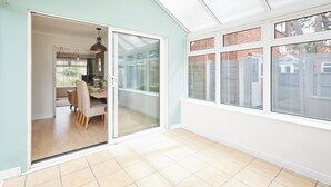 A bright room with a sliding glass door leading to a dining area, large windows, and a tiled floor. - Chester home only 2km from famous Races and Roman City, sleeps 6 by Restfully (Chester)