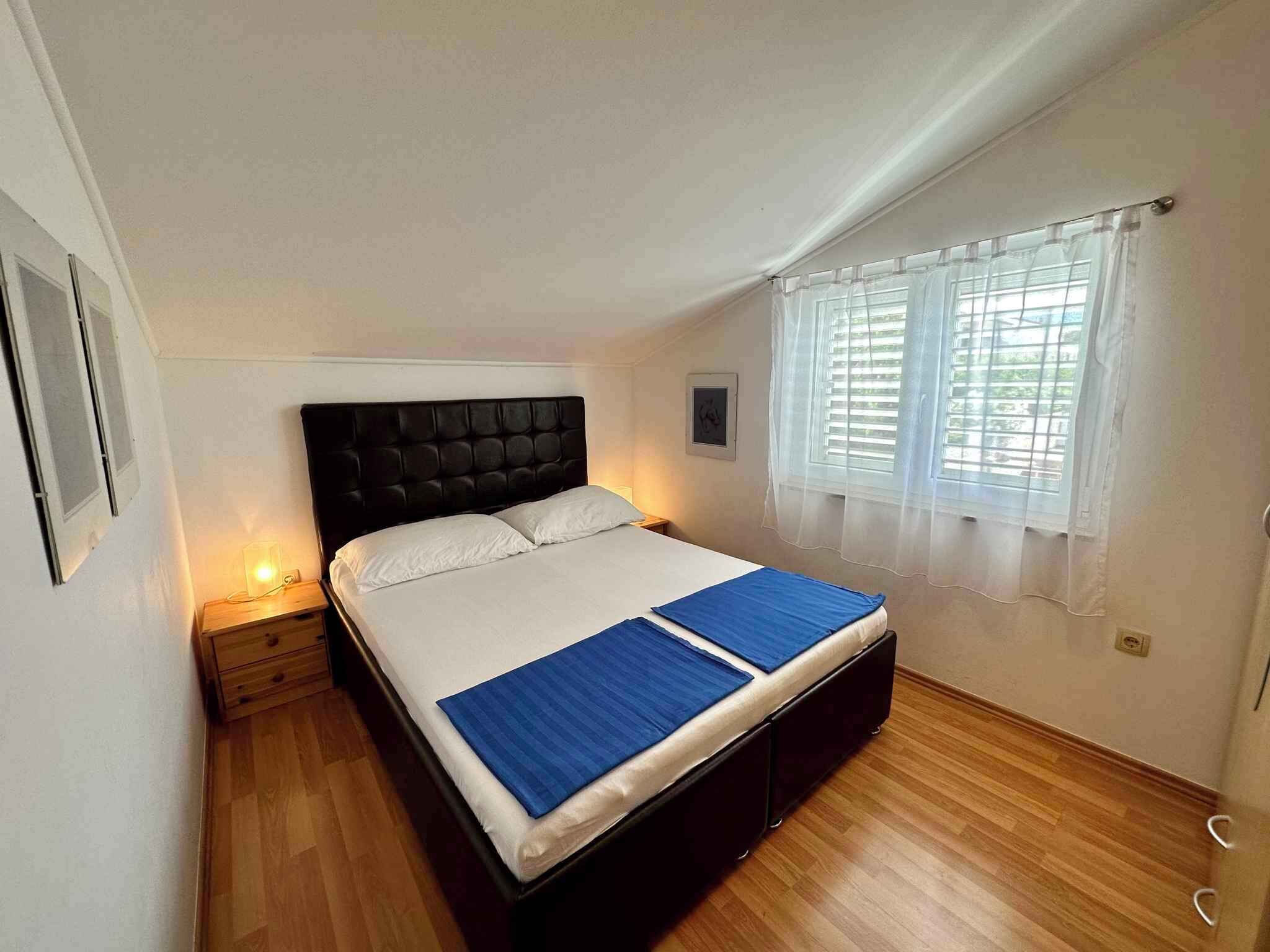 A bedroom with a bed, a nightstand, a window with curtains, and a wooden floor.