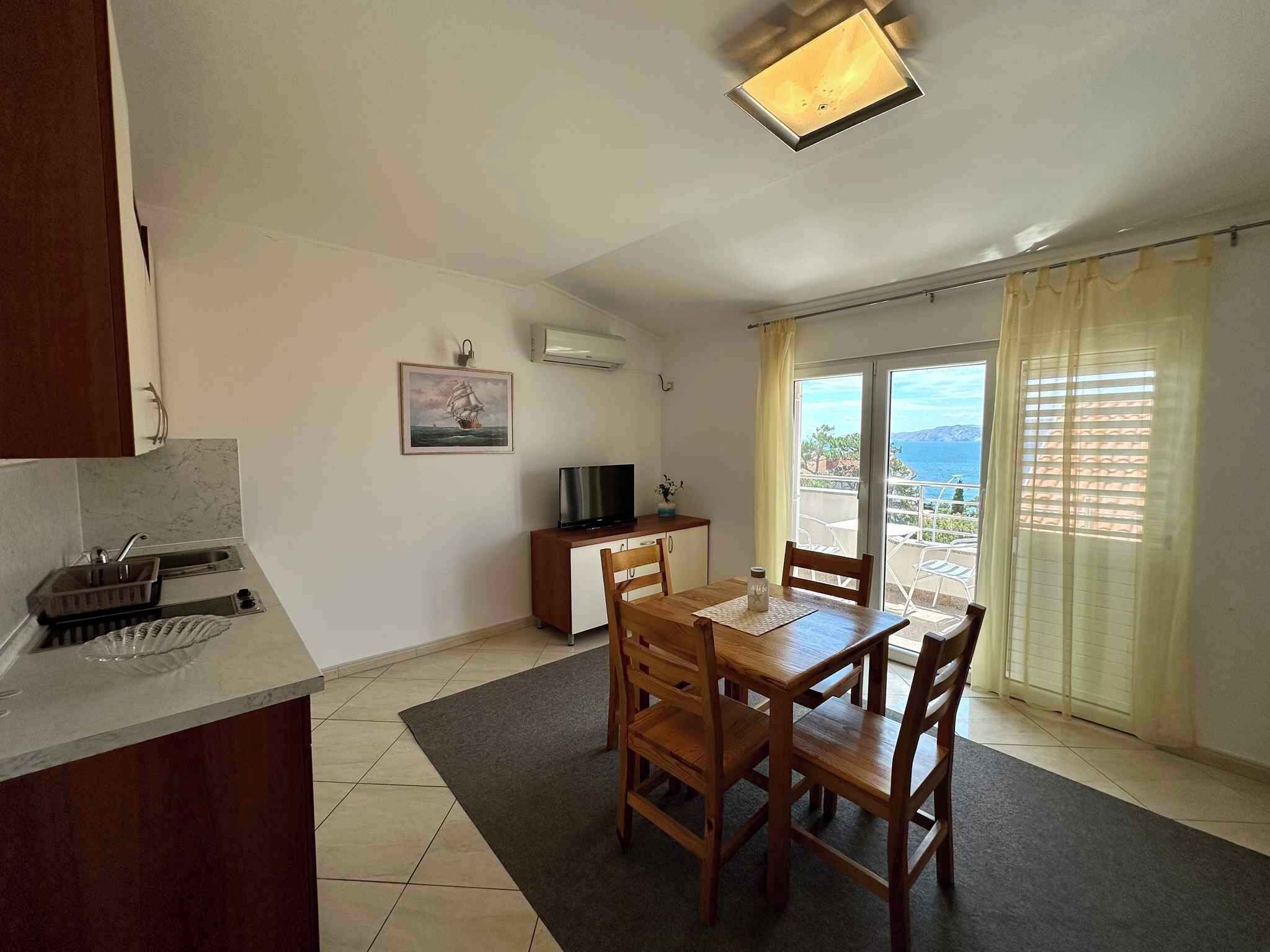 A compact living space with a dining area, kitchenette, and a large sliding glass door leading to a balcony with a scenic view.