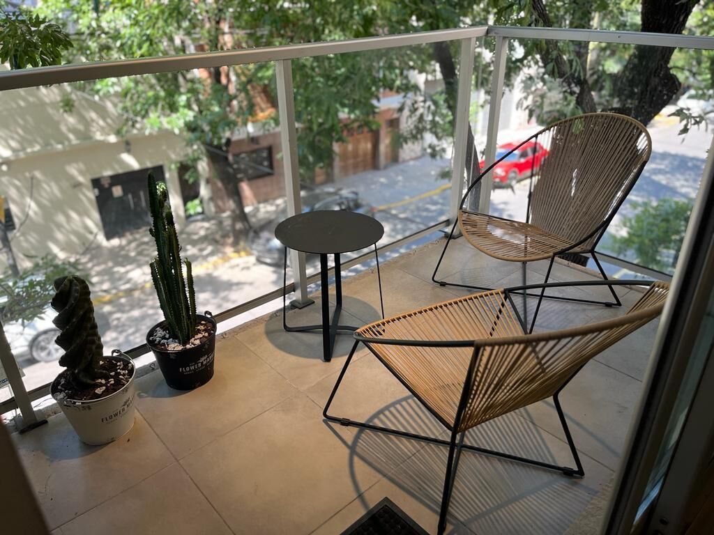 A balcony with two wicker chairs, a small round table, and two potted plants.