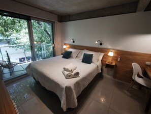 A neatly made bed with a rolled towel, two bedside lamps, and a view of the outdoors through a large window.