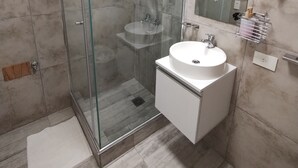 A modern bathroom with a glass-enclosed shower, a white sink, and a large mirror. - Estudio en Palermo III (Buenos Aires)