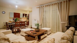 Ein Wohnzimmer mit einer Couch, einem Couchtisch und einem Fernseher. Es gibt einen Essbereich mit Stühlen und einem Tisch.
