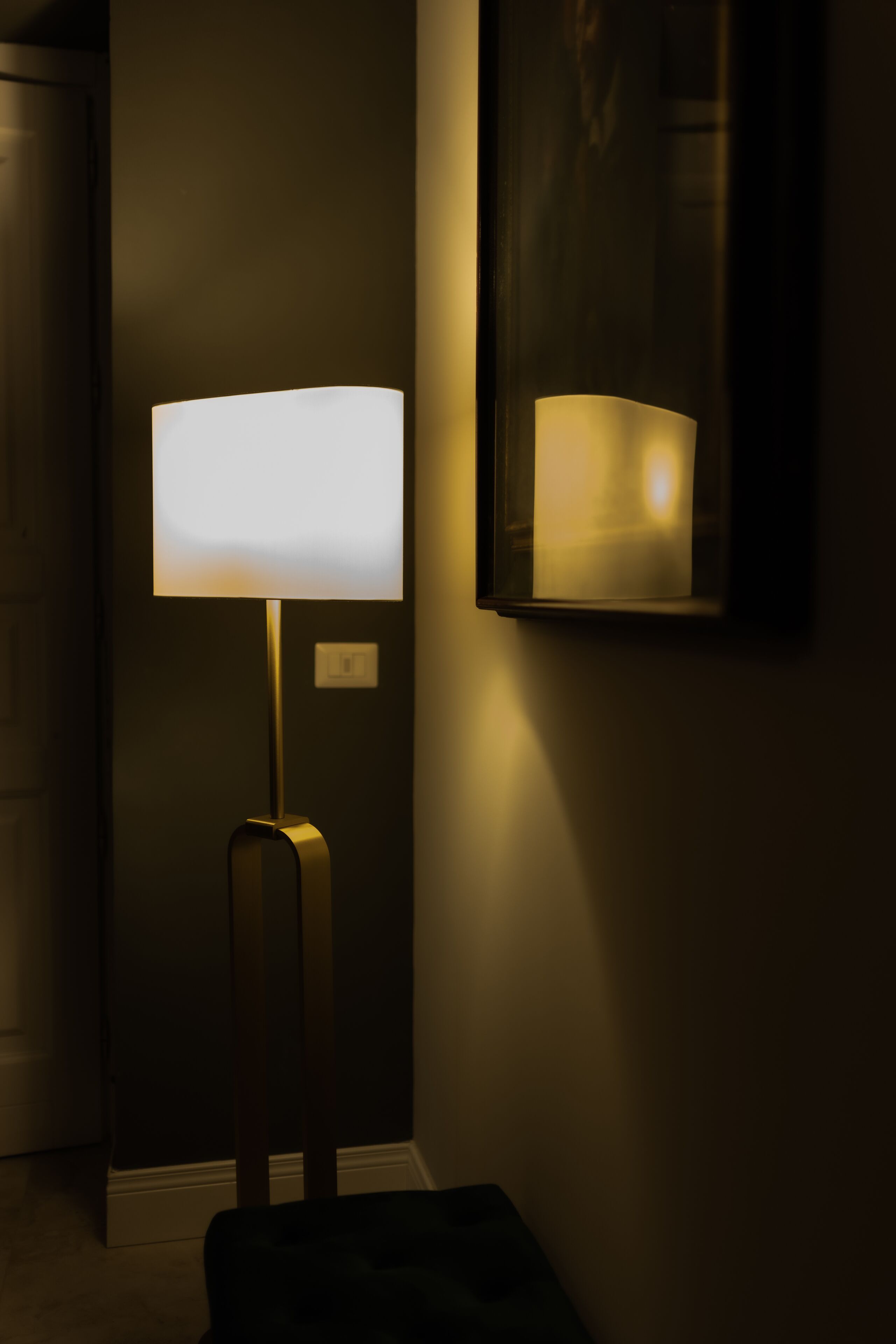 A modern floor lamp with a rectangular shade, positioned against a dark wall with a framed artwork above it.