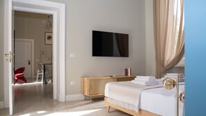 Een slaapkamer met een bed, een aan de muur bevestigde televisie, een radiator en een deur die naar een andere kamer leidt.