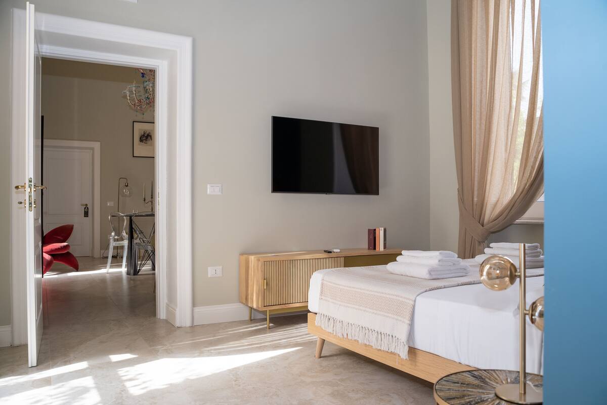 Ein Schlafzimmer mit einem Bett, einem an der Wand montierten Fernseher, einem Heizkörper und einer Tür zu einem anderen Raum.