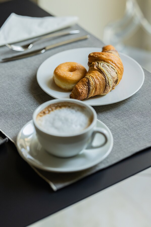 A plate with a croissant and a donut, and a cup of coffee on a table.