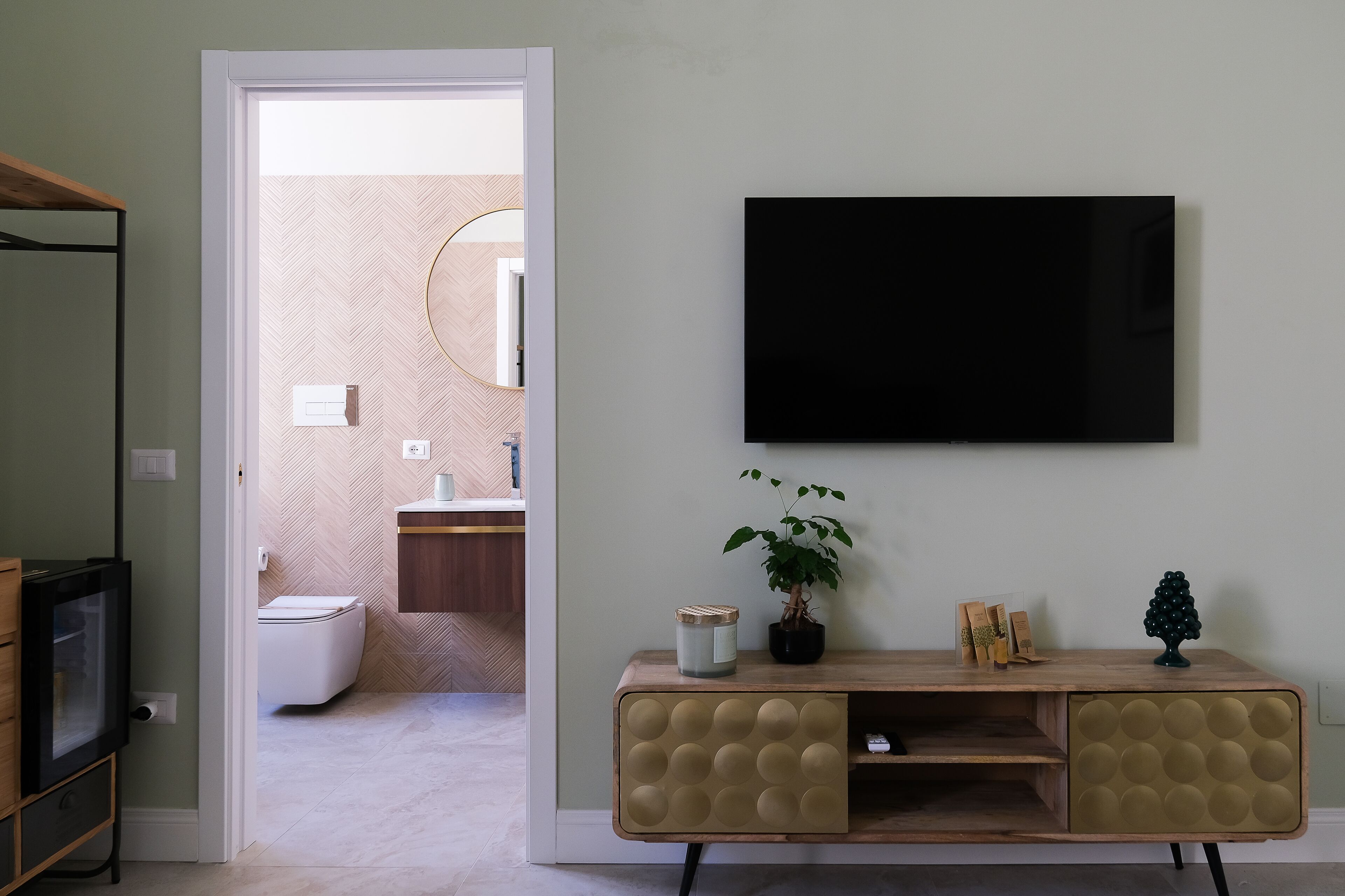 A modern living room with a television mounted on the wall, a wooden cabinet with decorative elements, and a potted plant.