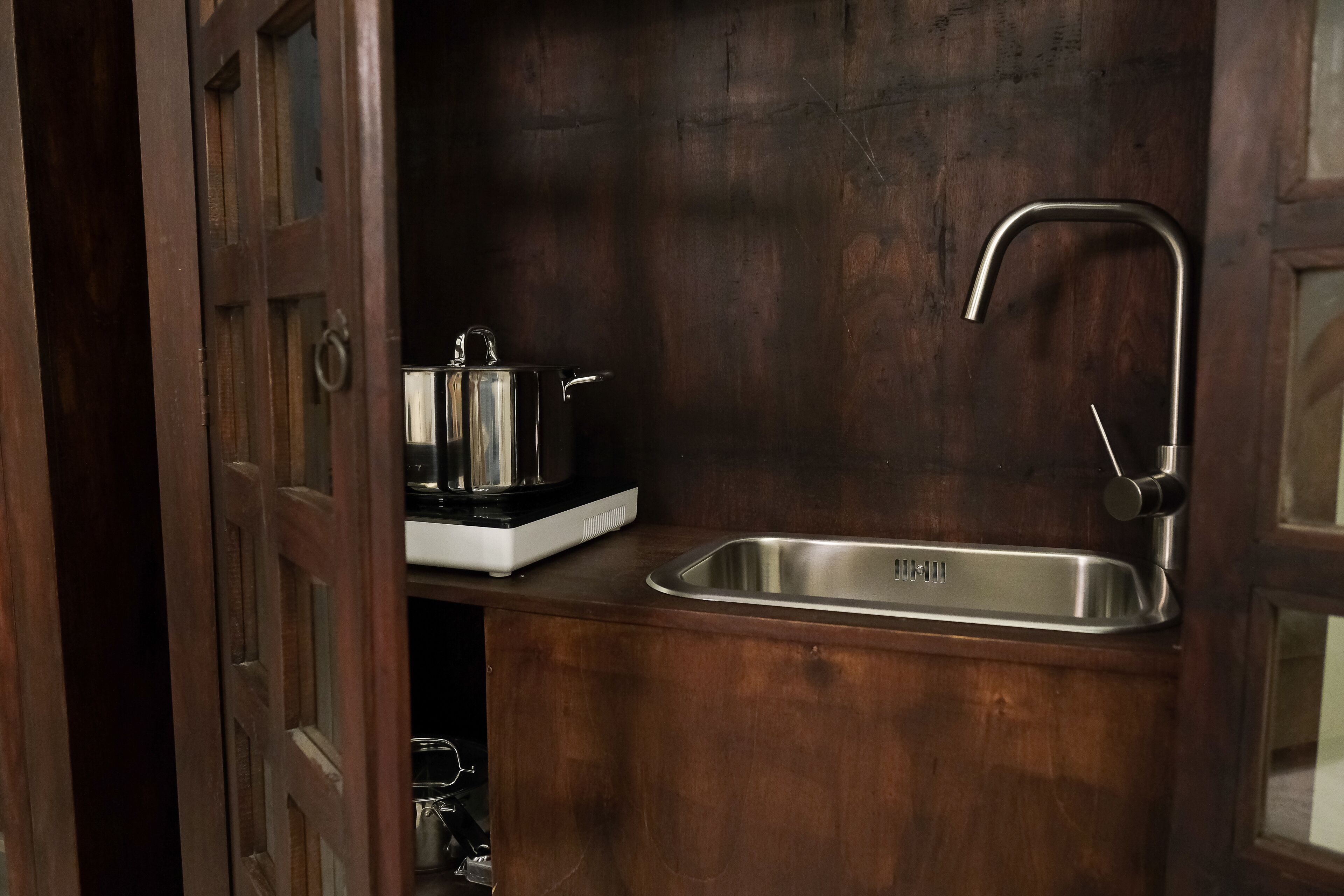 A kitchen with a stainless steel sink, a stove, and a wooden cabinet.
