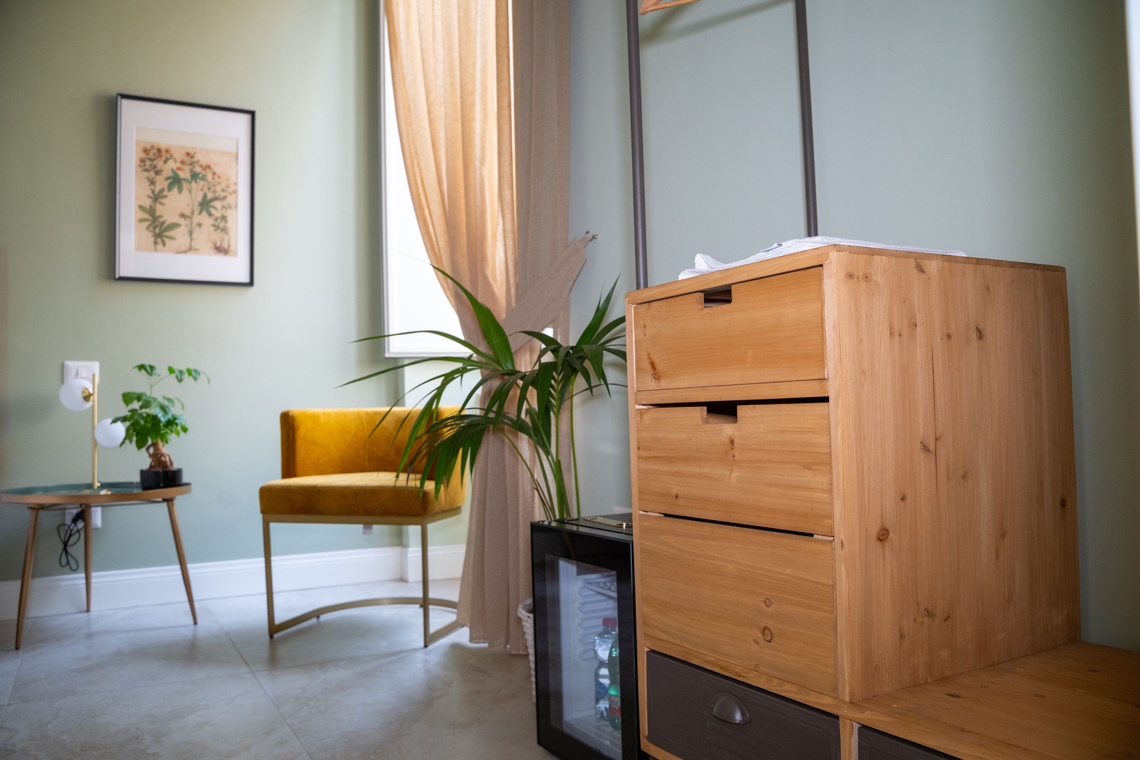 A room with a wooden dresser, a yellow chair, a potted plant, and a framed picture on the wall.