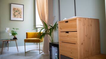 A room with a wooden dresser, a yellow chair, a potted plant, and a framed picture on the wall.