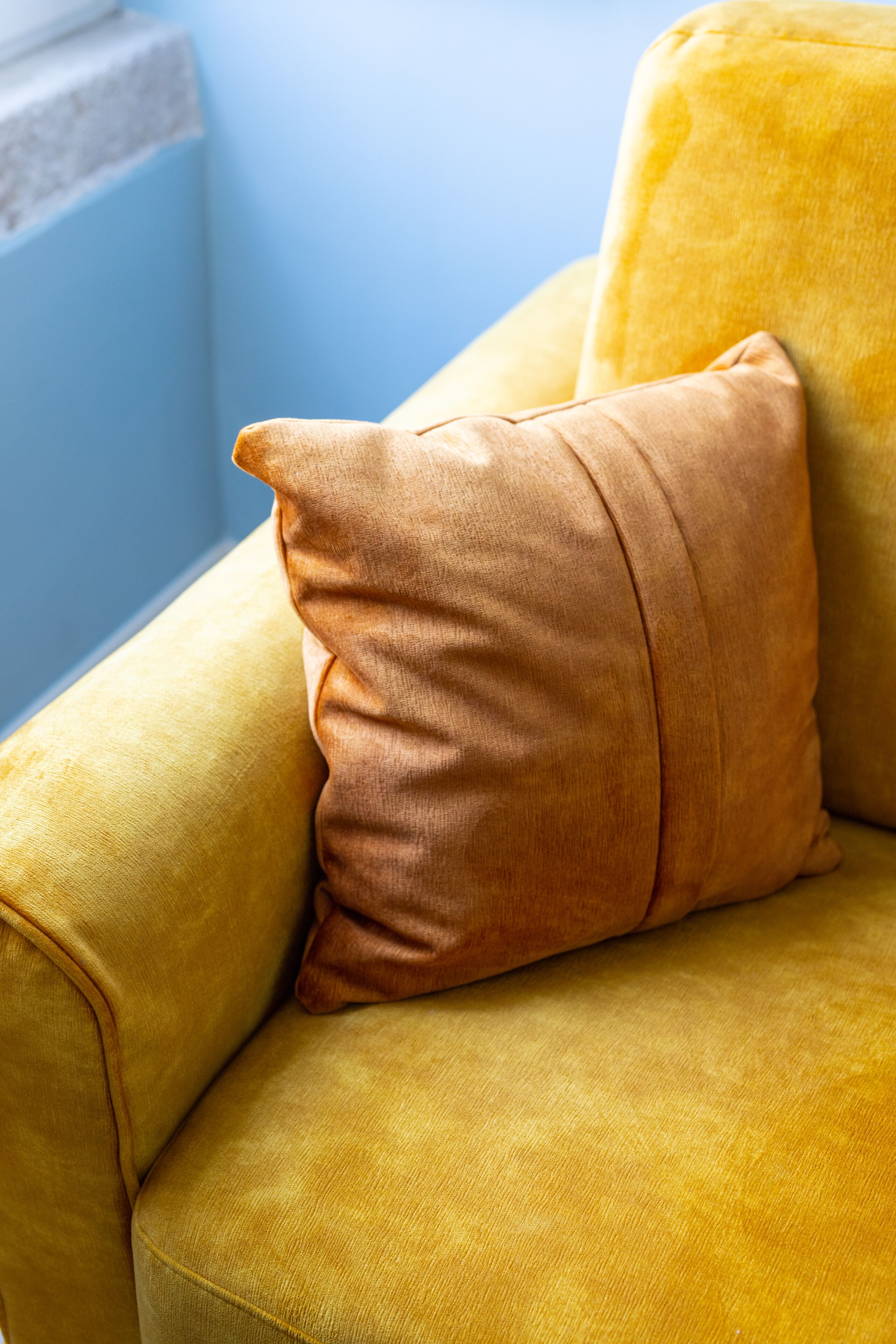 A yellow armchair with a single brown cushion.