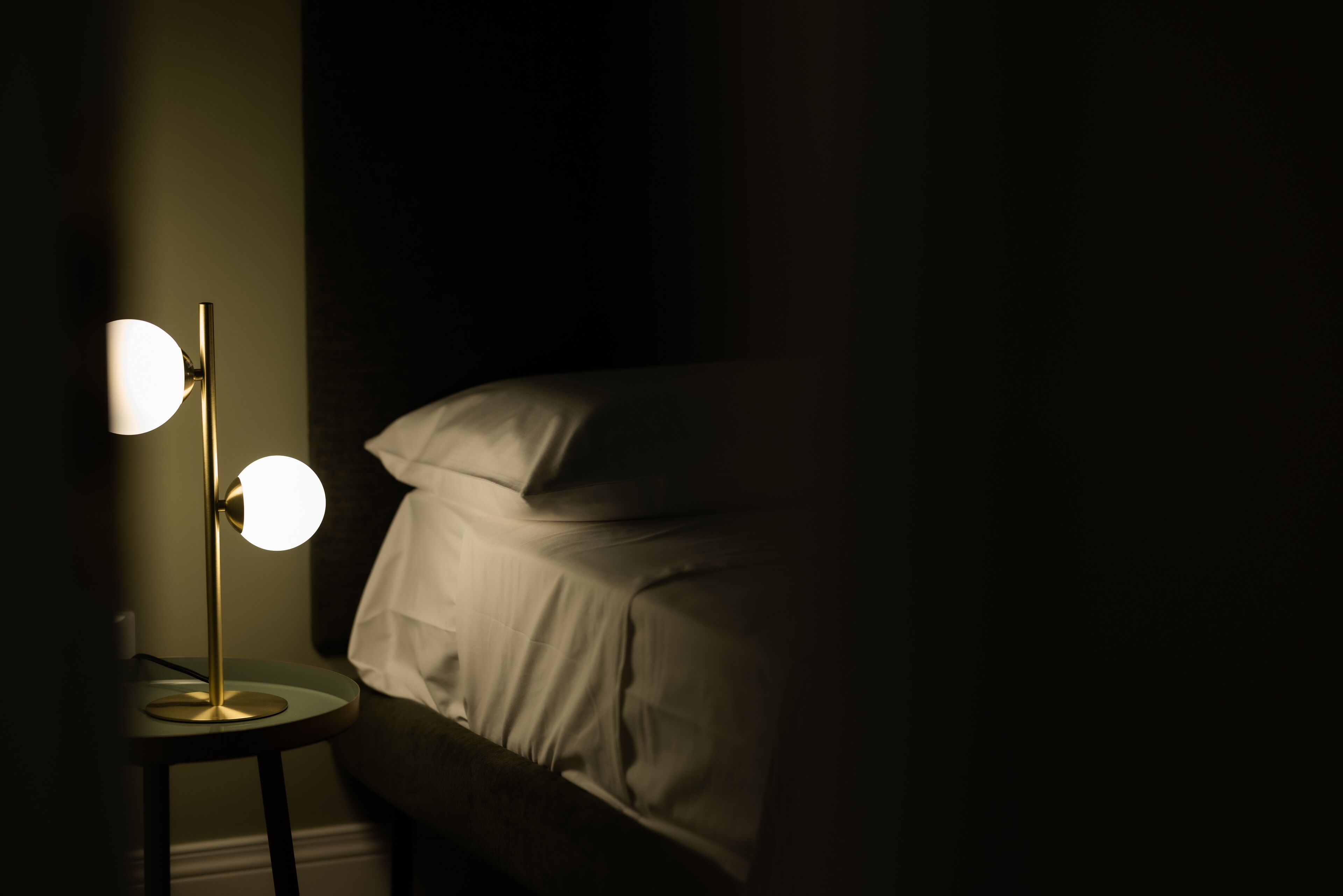 Una cama con ropa blanca y una mesita de noche con lámpara.