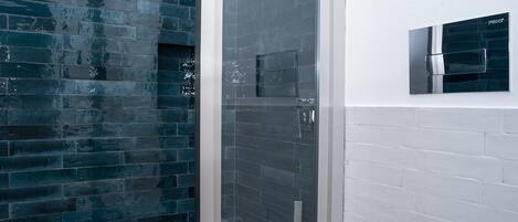 Un baño con cabina de ducha de vidrio, pared con azulejos blancos y pared con azulejos azul oscuro.