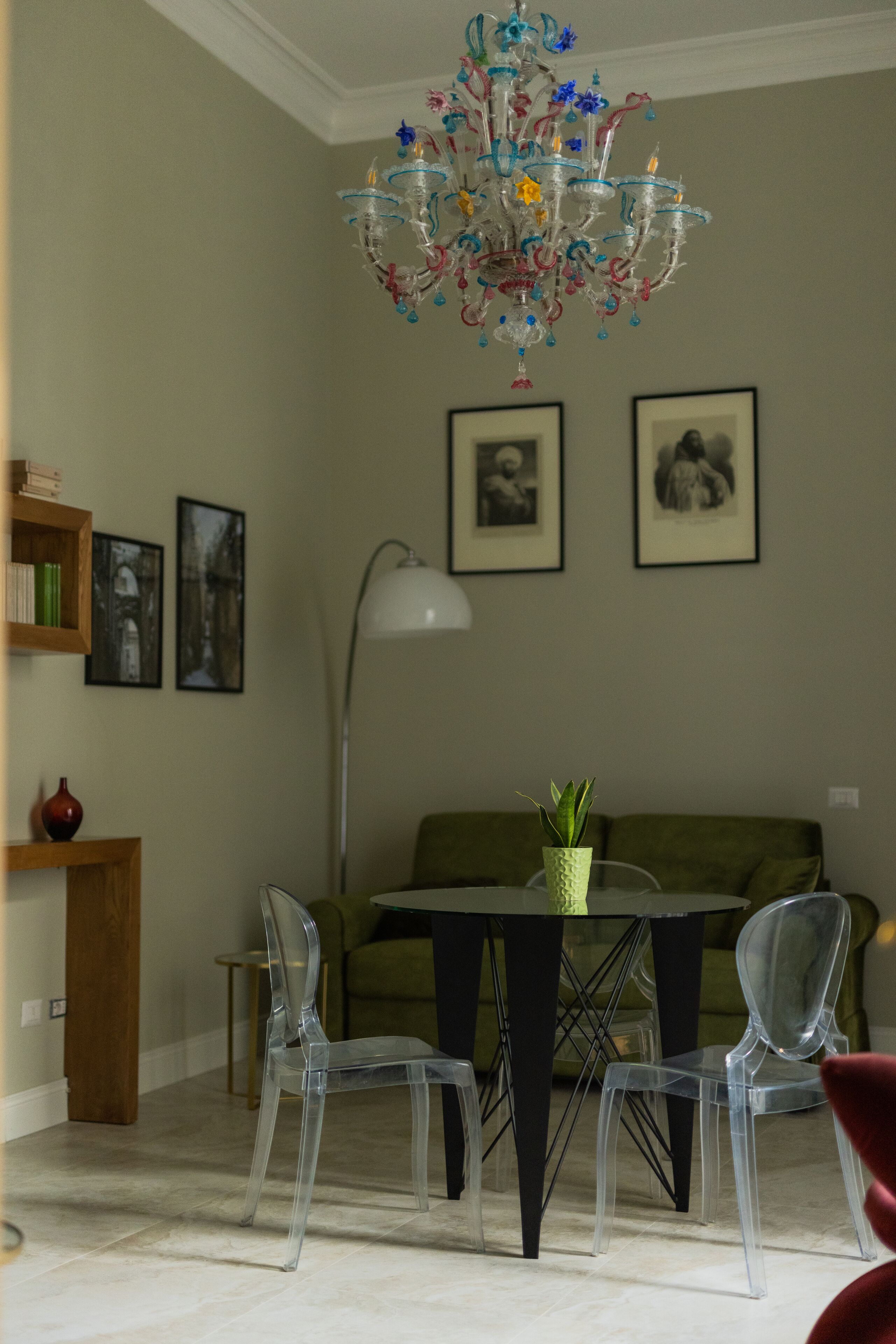 A dining area with a chandelier, clear chairs, a table, and framed pictures on the wall.