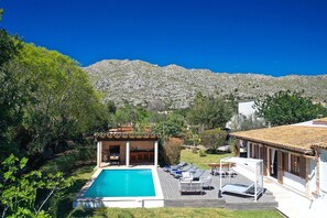 A pool area with lounge chairs, a pergola, and a view of a mountainous landscape.