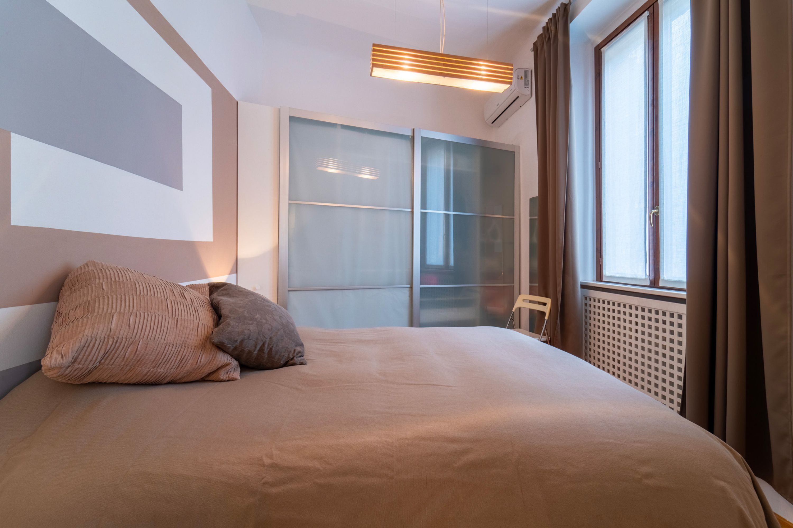 Una camera d'albergo moderna con un letto grande, un armadio con ante scorrevoli in vetro e una finestra con tende.