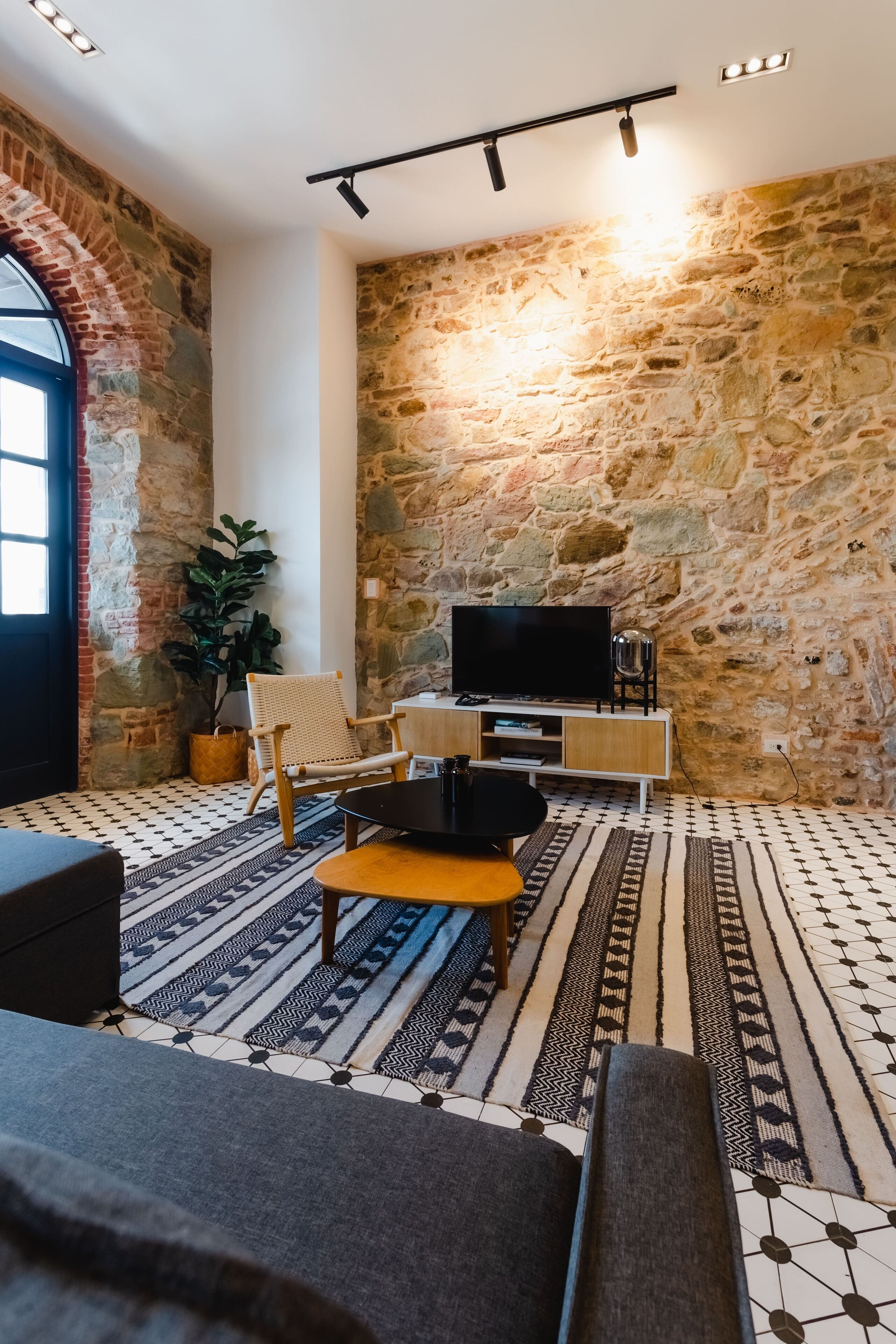 Una sala de estar acogedora con pared de piedra, televisor, sillón tejido y alfombras estampadas.