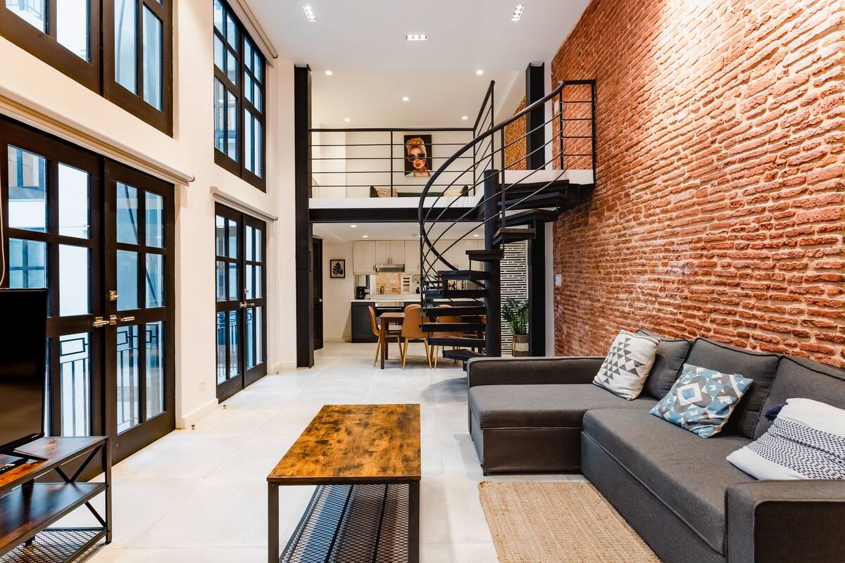 Un vaste espace de vie agrémenté d’un canapé moderne, d’une table basse en bois et d’un escalier menant à un niveau supérieur.