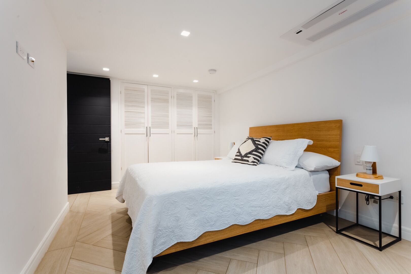 Un dormitorio con una cama, una mesita de noche con lámpara y un armario con puertas batientes.