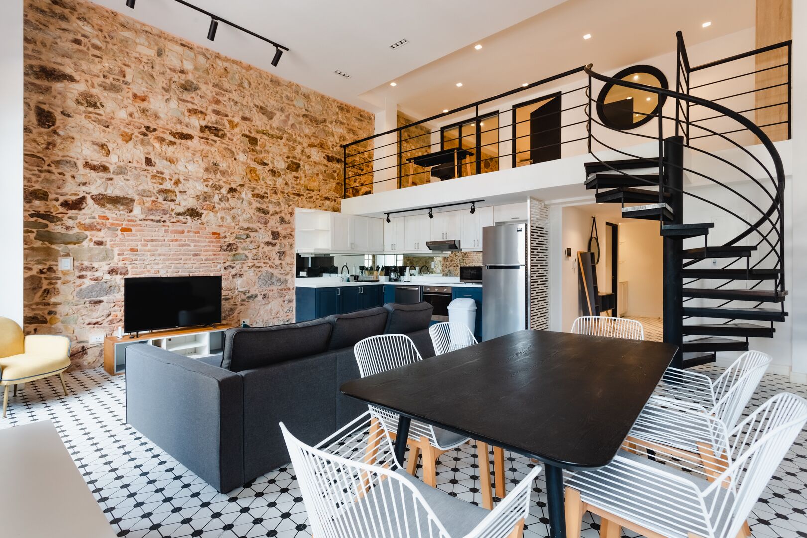 A modern living space with a stone wall, a dining area with a black table and white chairs, and a kitchen in the background.