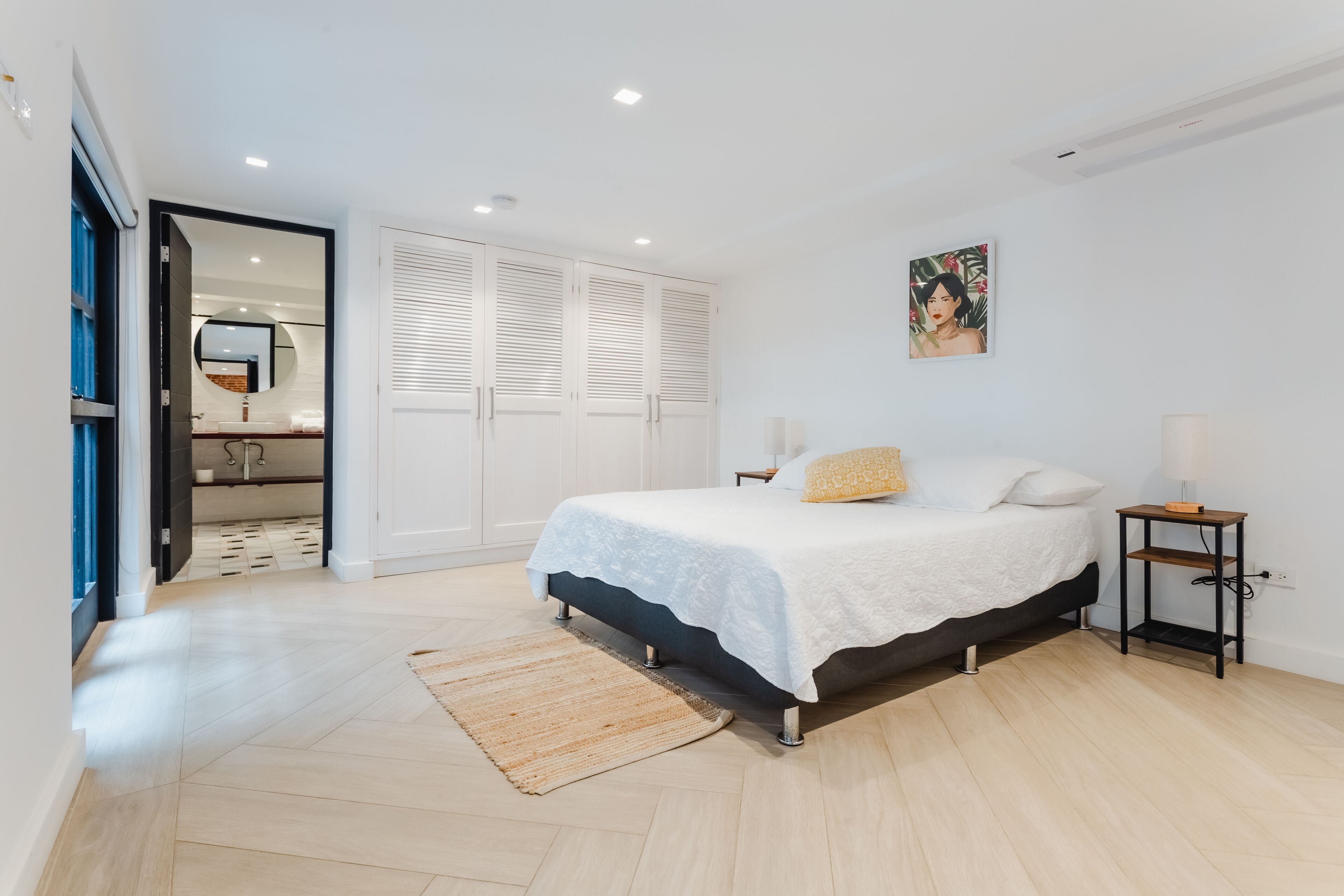 A bedroom with a bed, a bedside table, a lamp, and a painting on the wall.