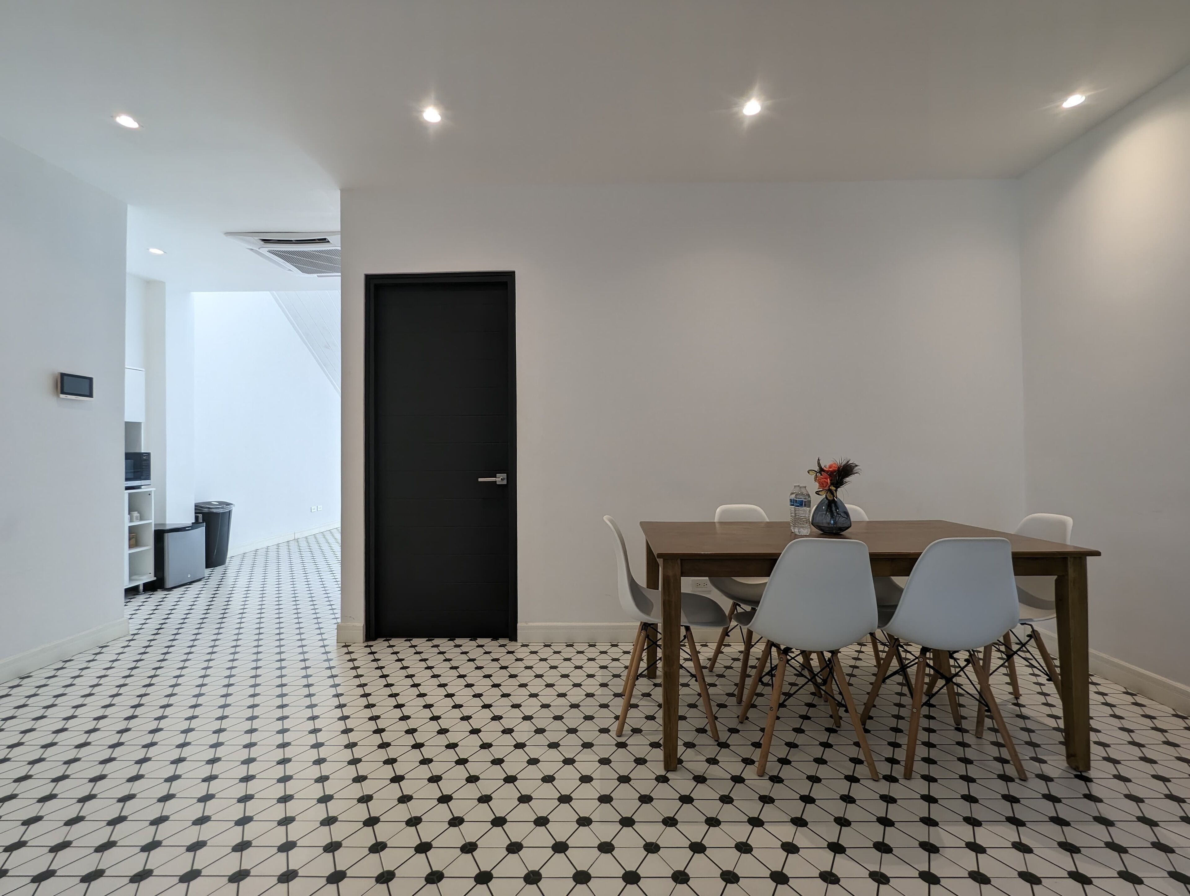 A dining area with a black door, white walls, and a tiled floor.