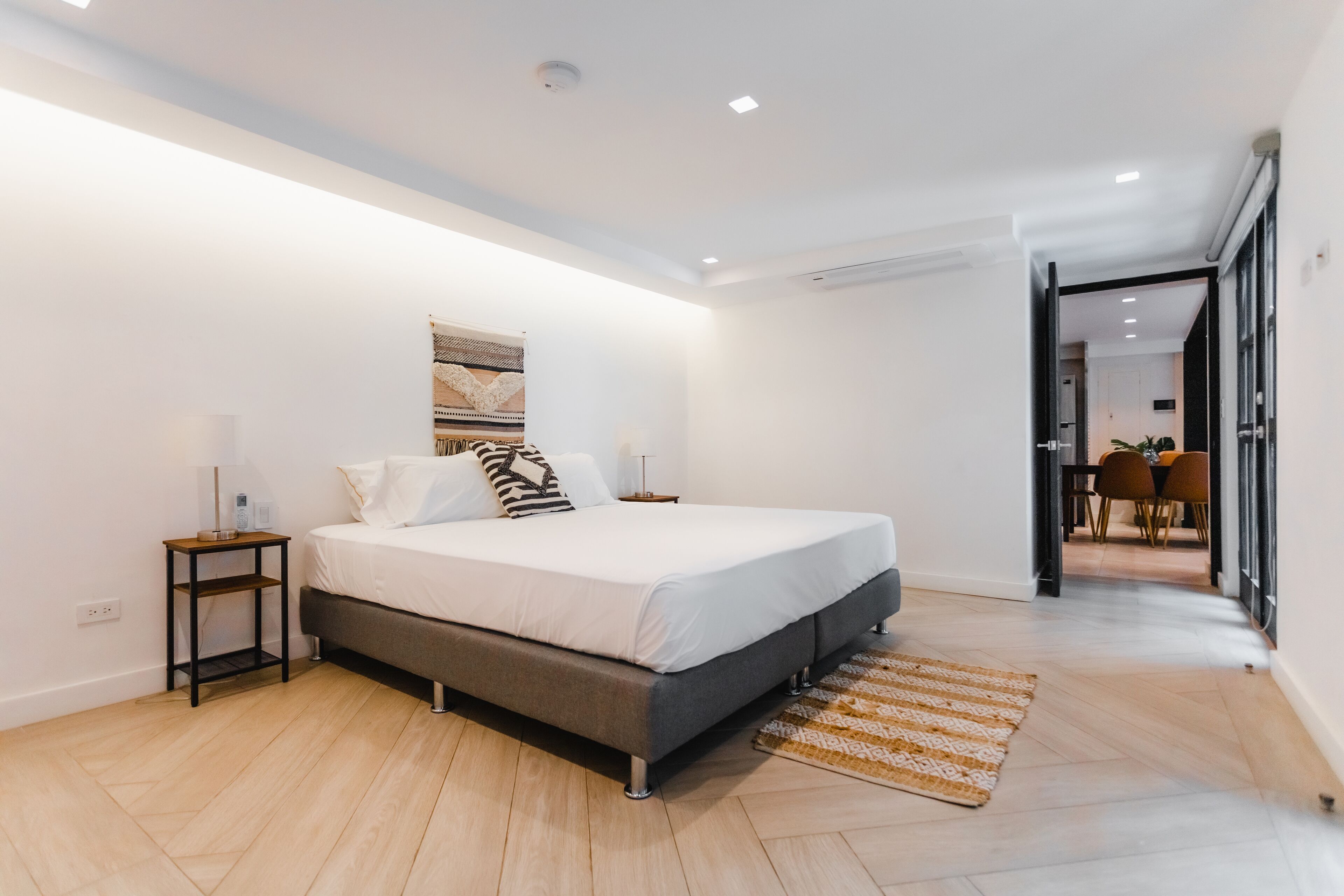 Un dormitorio moderno con una cama grande, mesitas de noche y vistas al comedor.