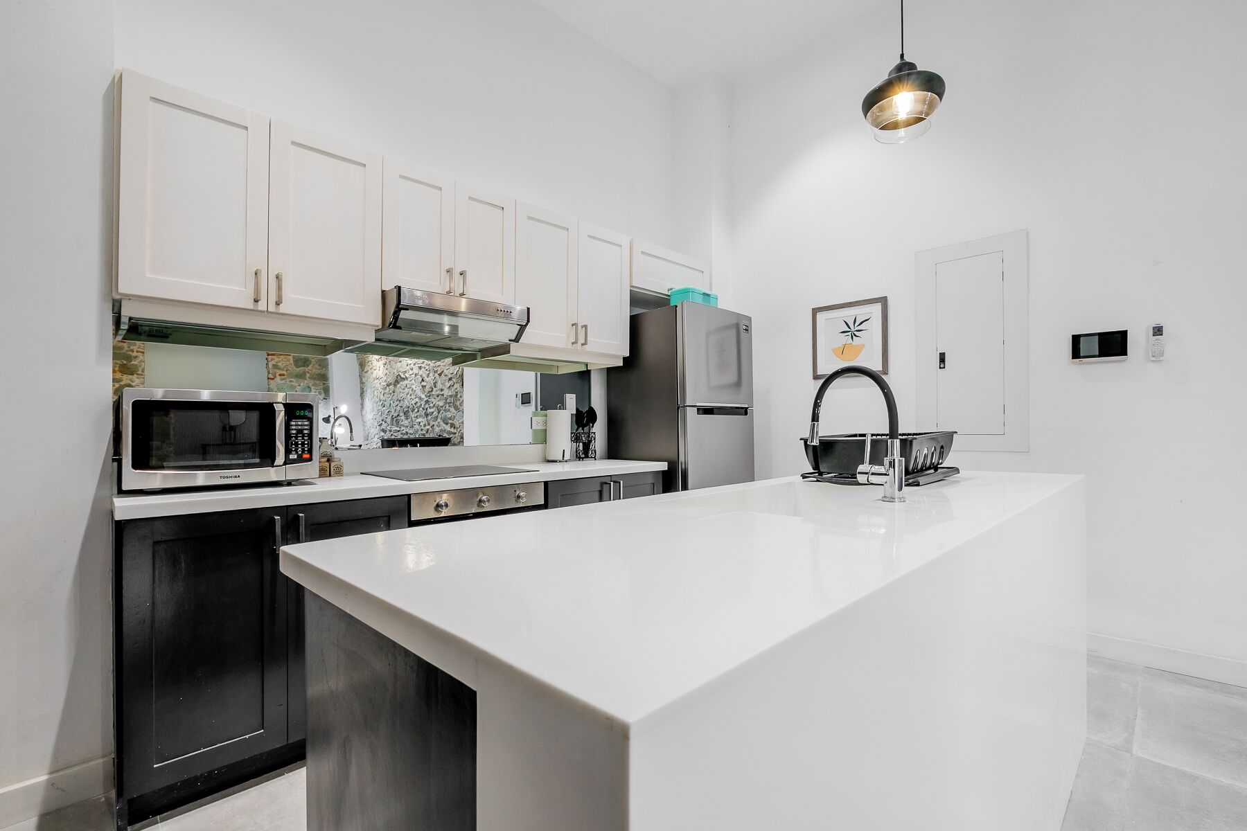 A modern kitchen with white cabinetry, a stainless steel refrigerator, a microwave, and a large island with a sink.