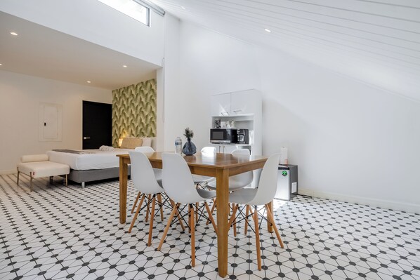 Una sala de estar moderna con un sofá, una mesa de comedor con sillas, una zona de cocina con armarios y un suelo estampado.
