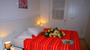 Ein ordentlich gemachtes Bett mit einer rot-weiß gestreiften Tagesdecke, weißen Kissen und einem Blumenstrauß aus gelben und weißen Blüten.