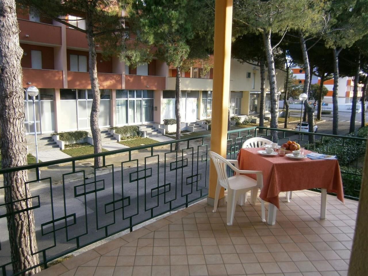 Un balcon avec une table et des chaises, donnant sur une cour intérieure bordée d’arbres et sur un bâtiment en arrière-plan.