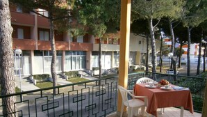 Un balcon avec une table et des chaises, donnant sur une cour intérieure bordée d’arbres et sur un bâtiment en arrière-plan.