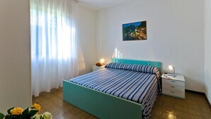 Une chambre à coucher avec un lit, une table de chevet, une lampe, un tableau et une fenêtre avec des rideaux.
