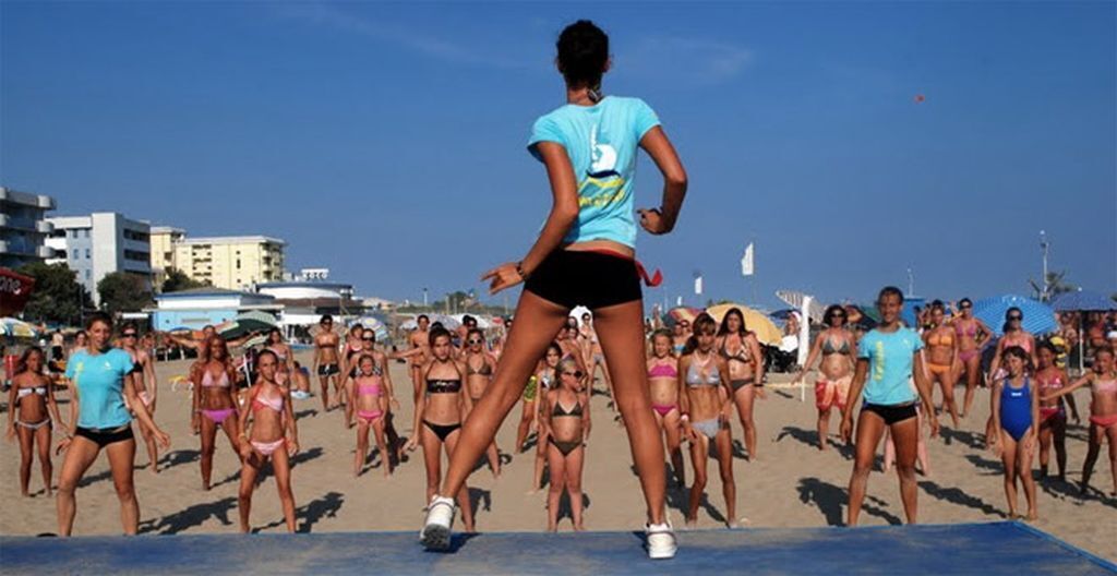 Ein Strand mit Personen in Badekleidung, einem klaren Himmel und Gebäuden im Hintergrund.