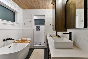 A modern bathroom with a freestanding bathtub, a large mirror, and a shower area. - Whitetail Run | Beautiful custom cabin 2BR + Loft sleeps 10 w/ hot tub (Broken Bow)