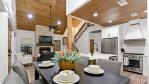 A dining area with a wooden table set for four, a fireplace, and a kitchen with modern appliances.