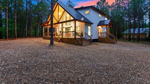 A cabin with a large porch, wooden stairs, and a gravel driveway surrounded by trees.