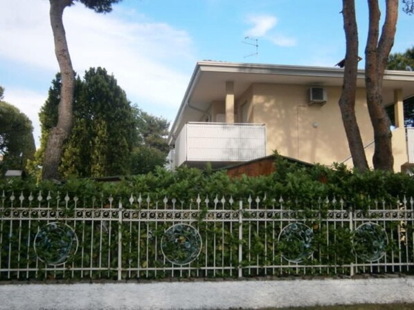 Un edificio de fachada color beige, con un balcón y una cerca blanca decorada con diseños circulares.