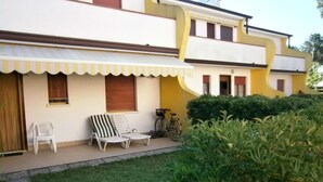 Un edificio con fachada amarilla y blanca, un porche cubierto con mobiliario exterior y una bicicleta estacionada afuera.