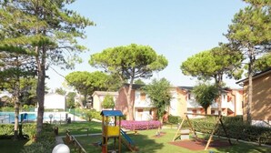Un parque infantil con toboganes y columpios, rodeado de árboles y una piscina.