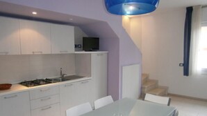 A modern kitchen with white cabinets, a dining table, and chairs. There is a blue pendant light above the table. - Residenz Silvida Wohnung A3 für 6 Personen (Bibione)