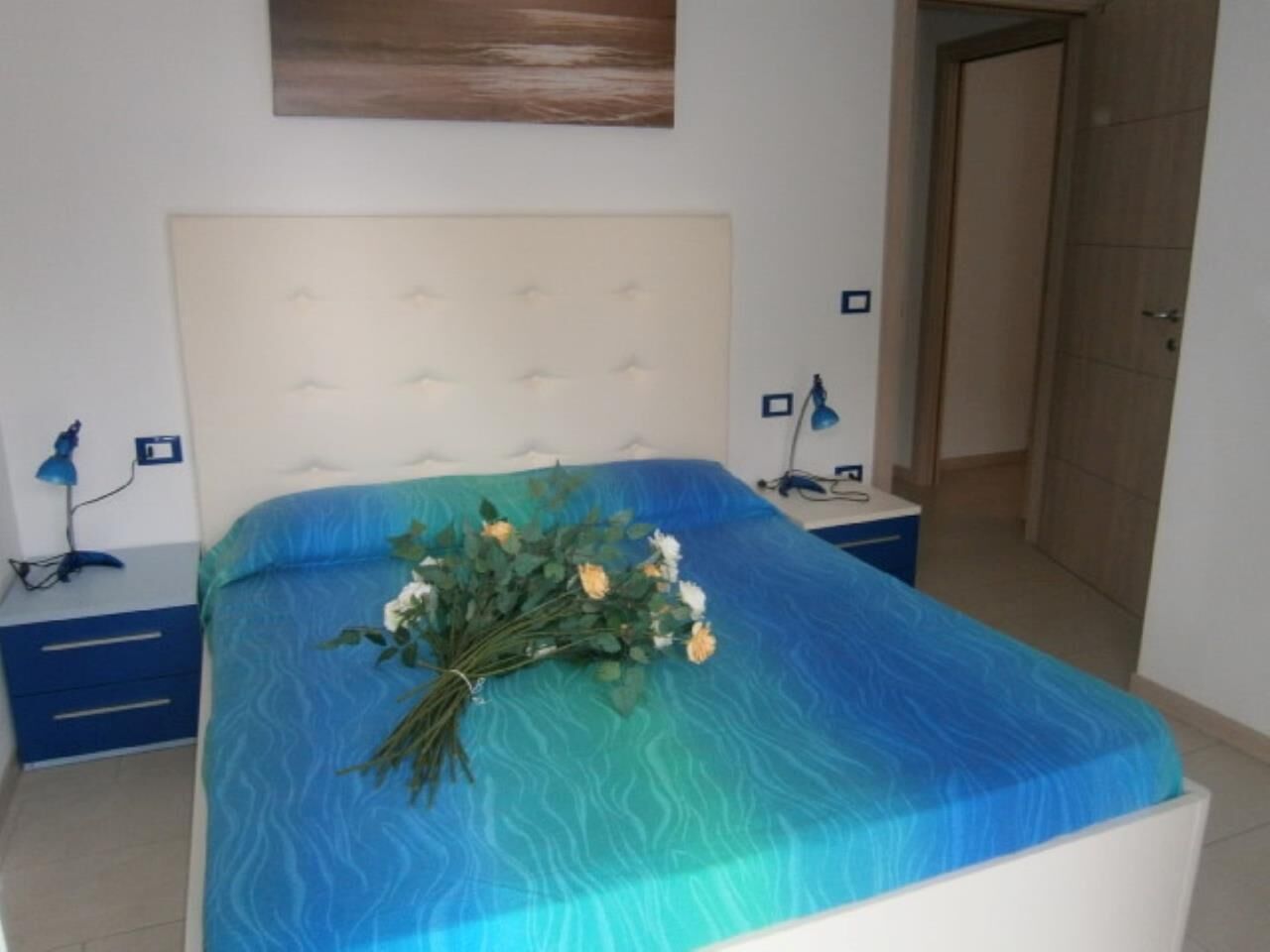 A bedroom with a bed, a nightstand, a lamp, and a door.