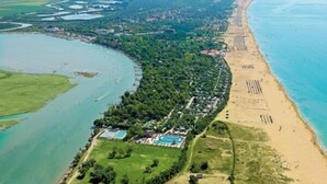 Oversigtsbillede af et kystområde med strand, swimmingpool og grøn bevoksning omkring.