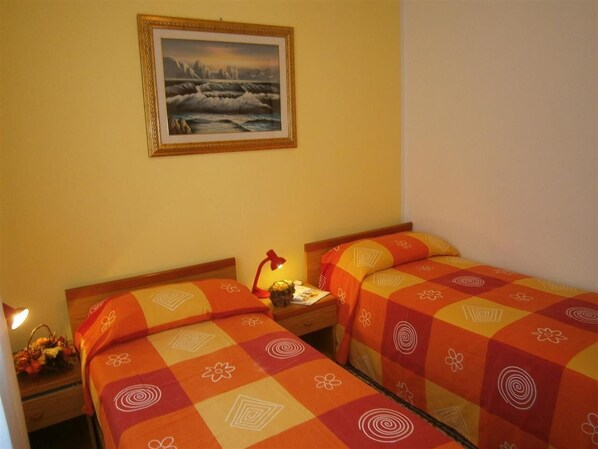 Una habitación con dos camas, cada una con una colcha estampada, una mesita de noche con lámpara y un cuadro en la pared.