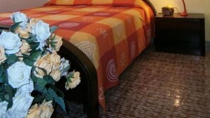 Un dormitorio con una cama, una mesita de noche, una lámpara, un cuadro enmarcado en la pared y un ramo de flores.